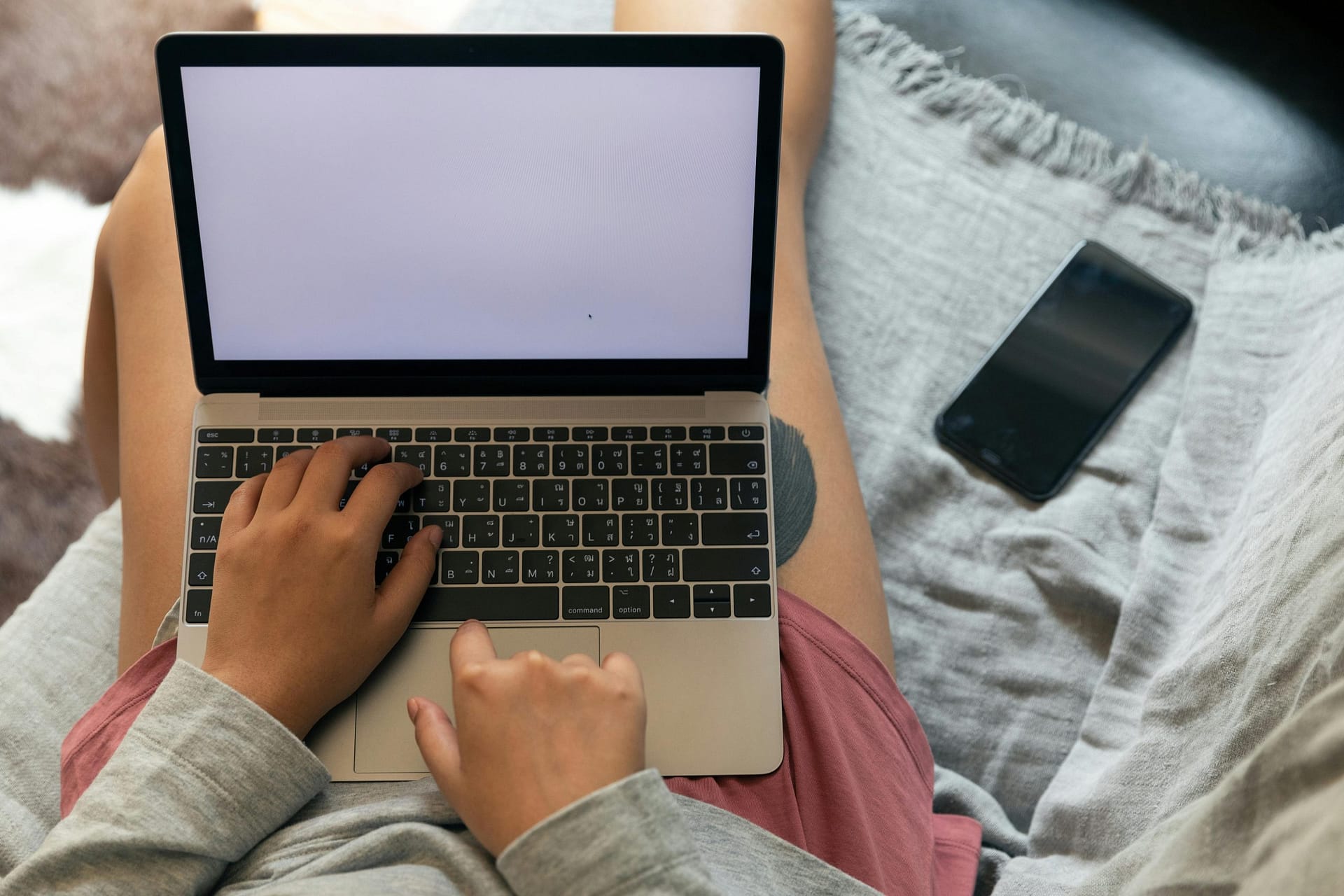 A person working remotely with a laptop on their lap and smartphone beside, showcasing modern work flexibility.