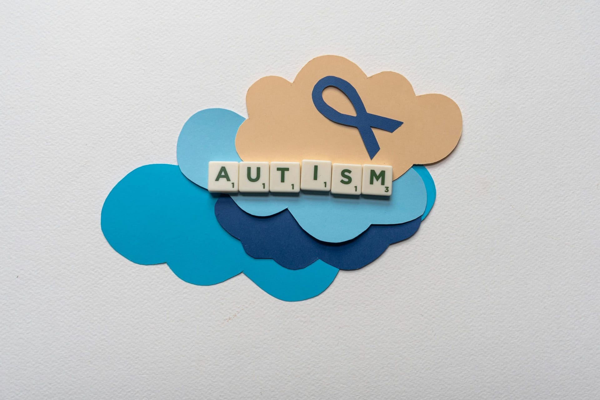 Creative representation of autism awareness using scrabble tiles on colorful clouds and ribbon.