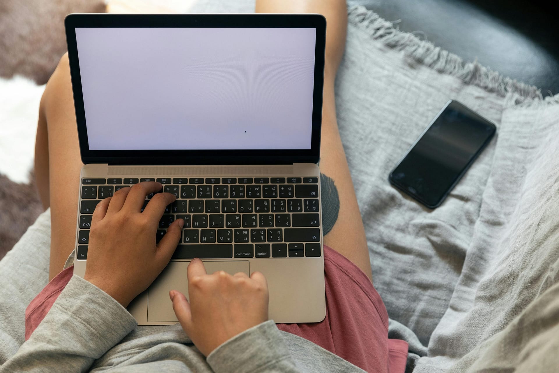 A person working remotely with a laptop on their lap and smartphone beside, showcasing modern work flexibility.