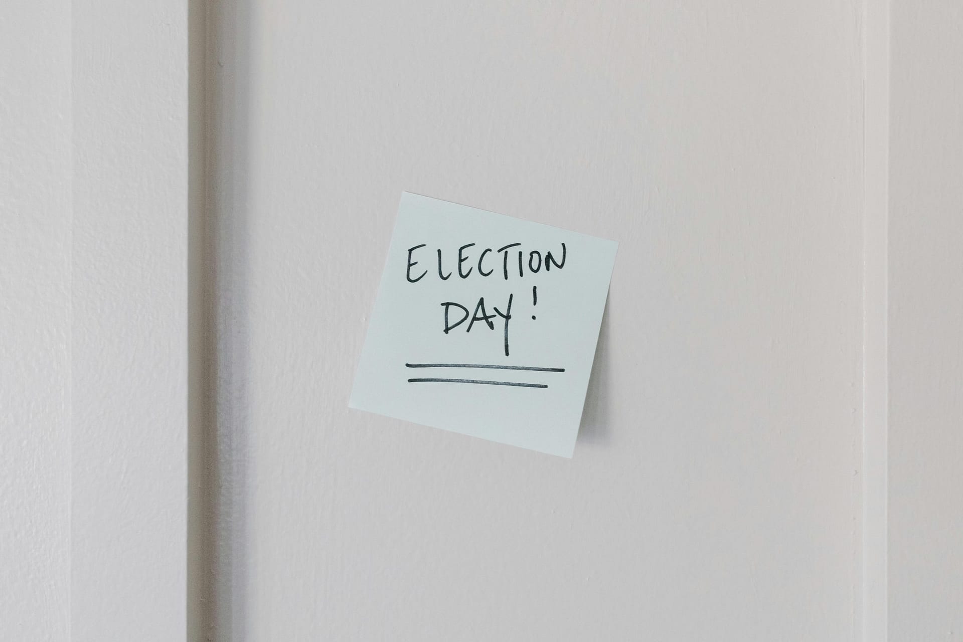 Sticky note with 'Election Day' message on a white wall background.