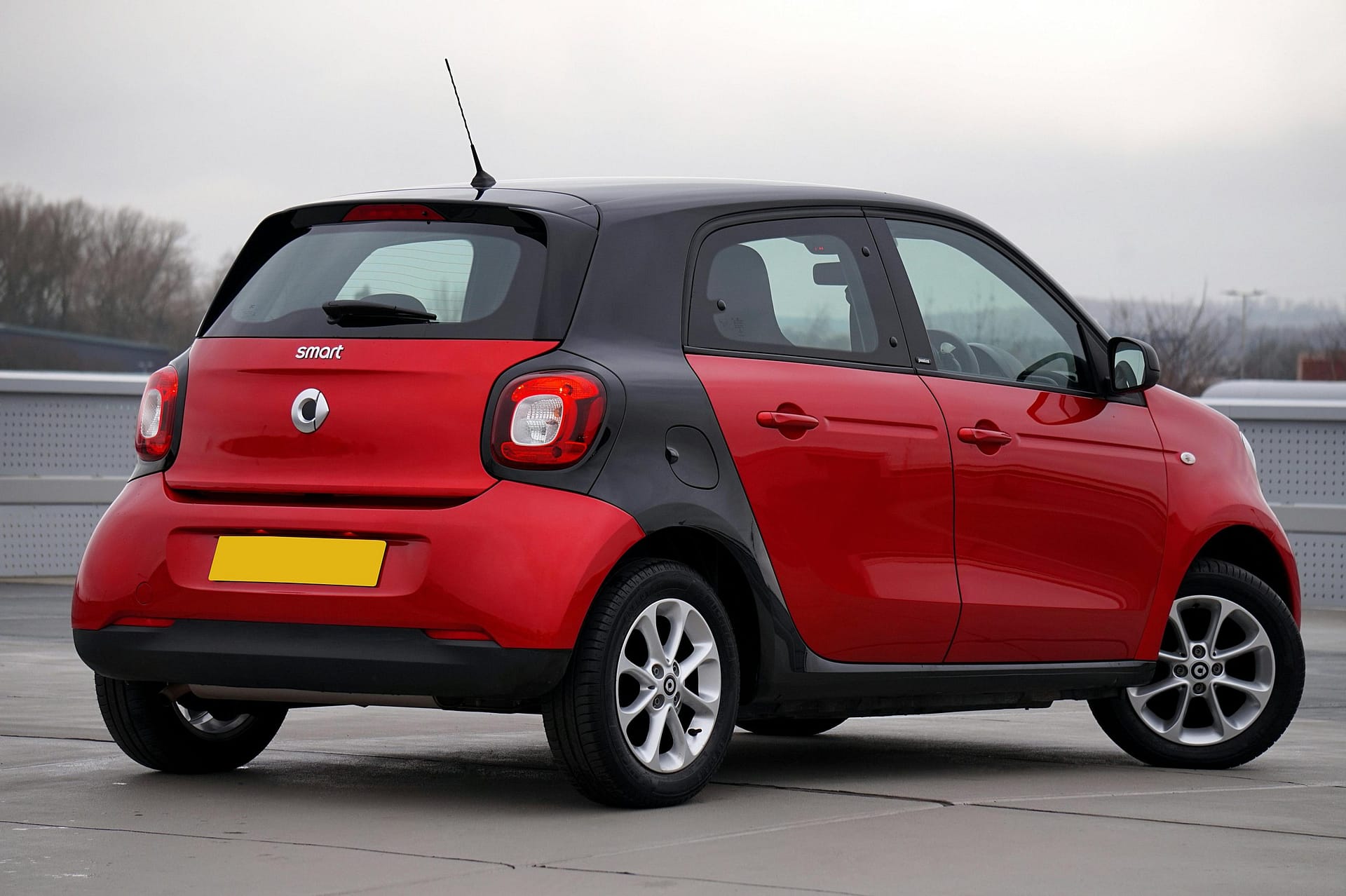 Rear view of a red Smart Forfour parked outdoors on a cloudy day, showcasing sleek design.